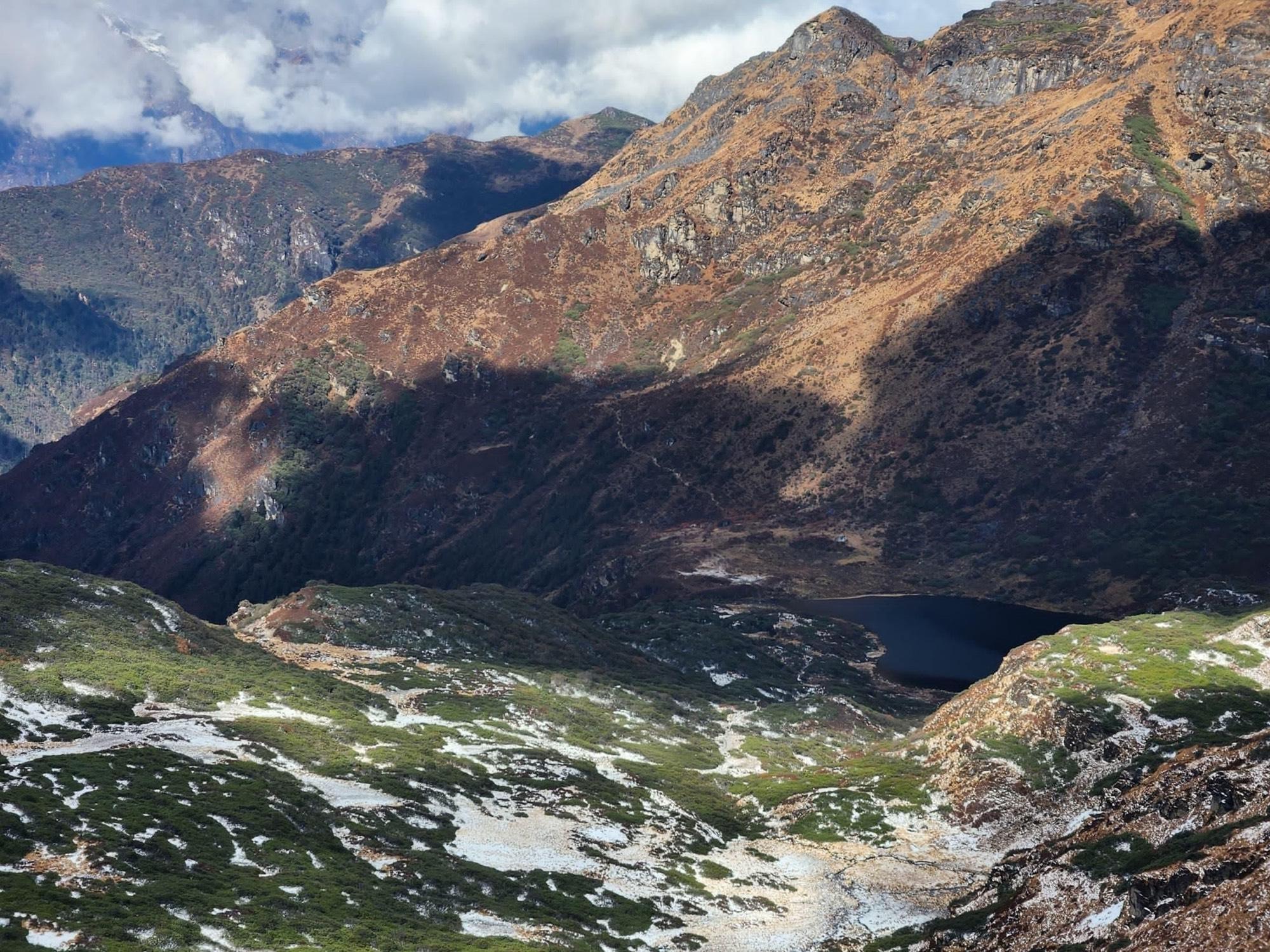 A dark alpine lake held between snow-dusted mountain slopes in Bhutan