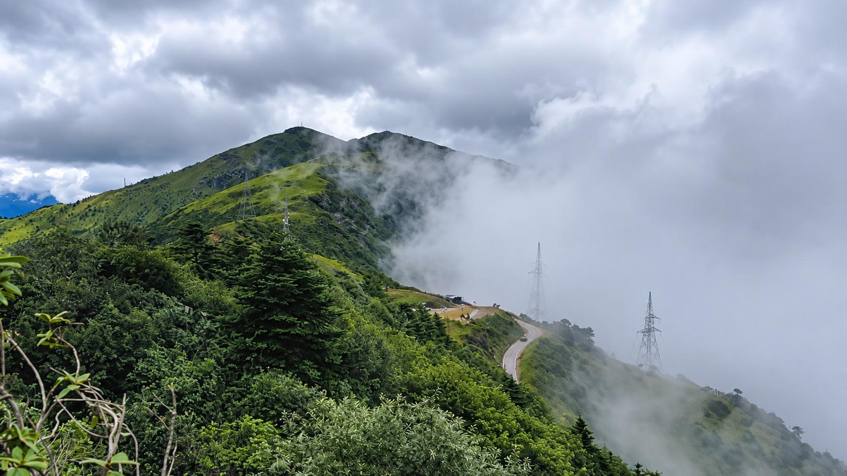 The winding road across a green ridge disappearing into cloud at Chele La Pass