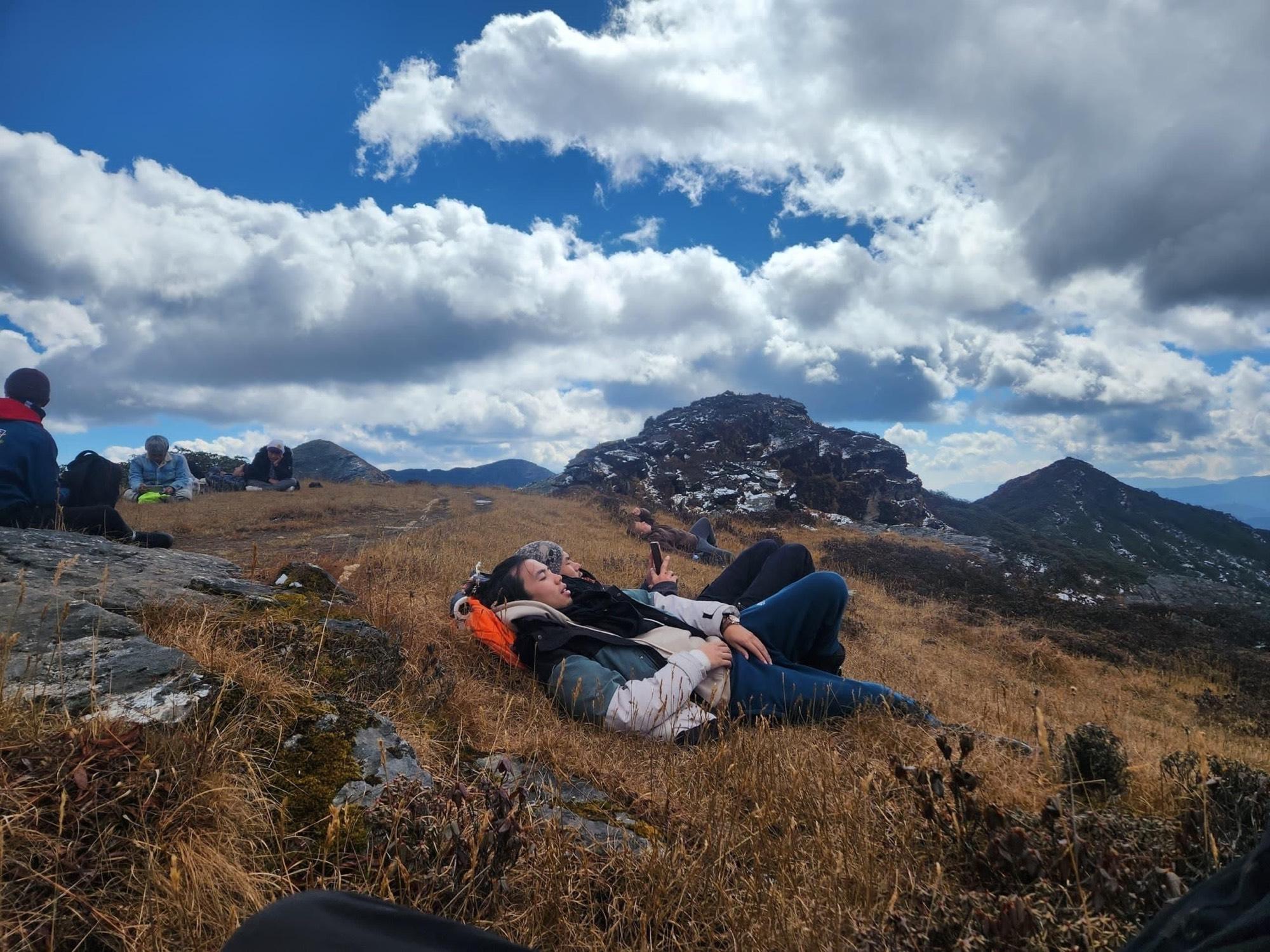 Travelers resting on an alpine ridge beneath cloud-filled skies en route to Dungtsho