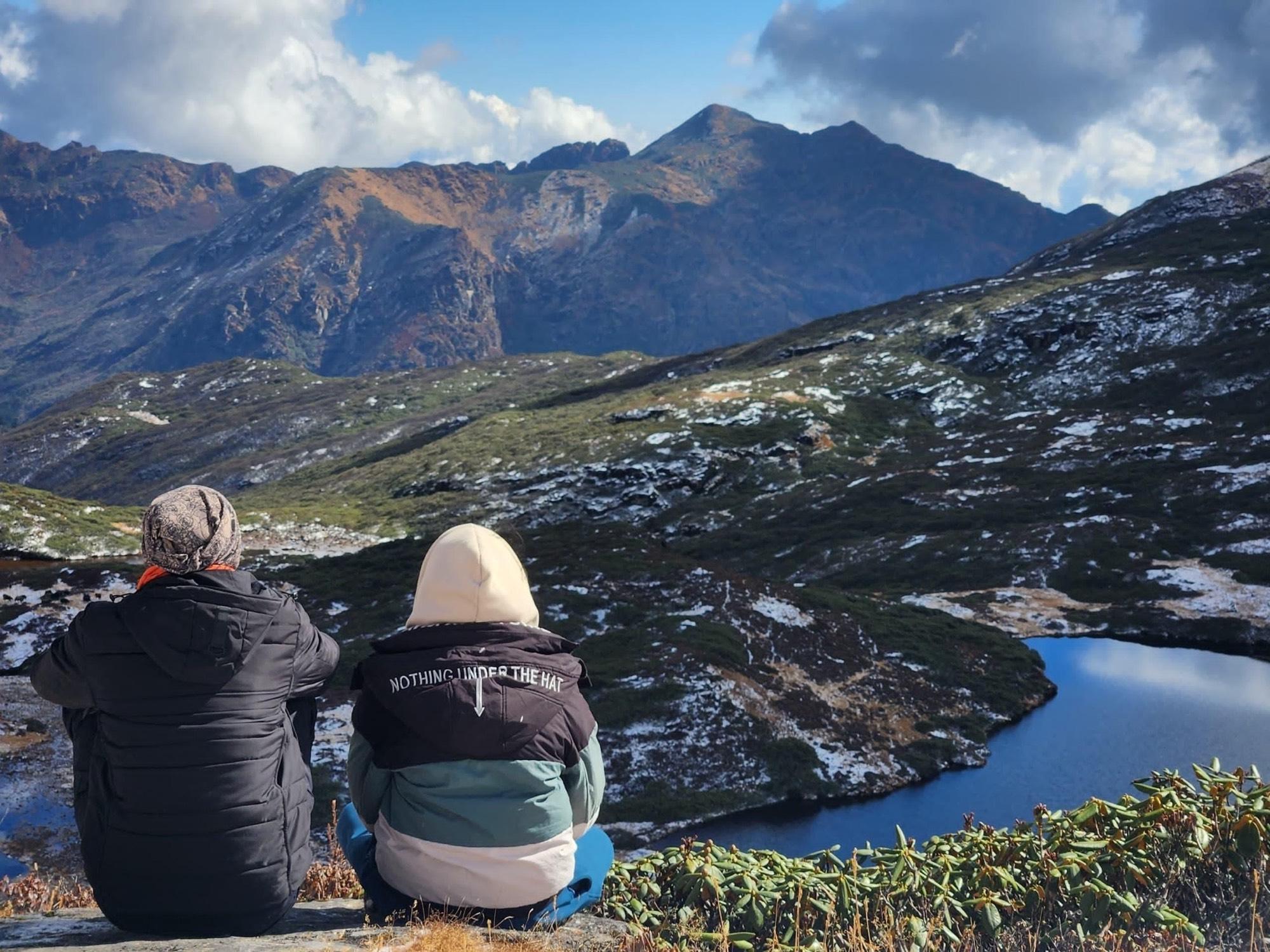 Two travelers sitting together above a snow-dusted alpine lake in Bhutan
